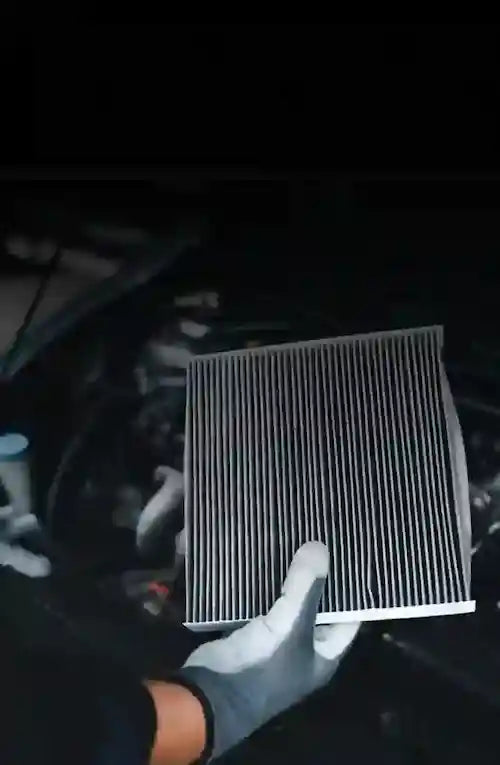 Mechanic holding a cabin air filter in front of the engine bay

